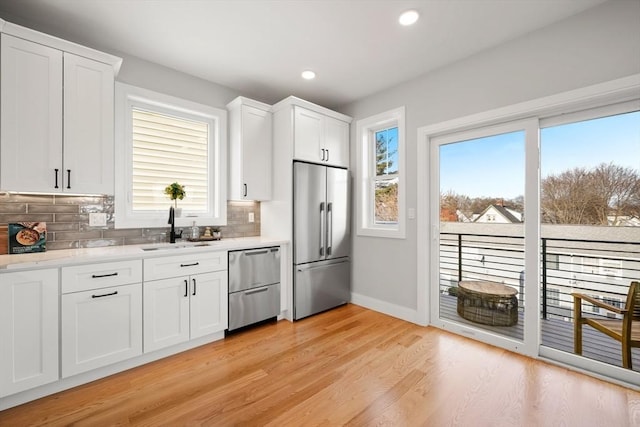 kitchen featuring light wood-style flooring, stainless steel appliances, a sink, white cabinets, and decorative backsplash