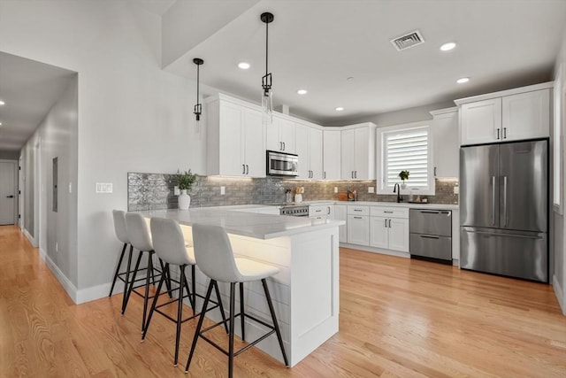 kitchen featuring a peninsula, visible vents, appliances with stainless steel finishes, light wood finished floors, and tasteful backsplash