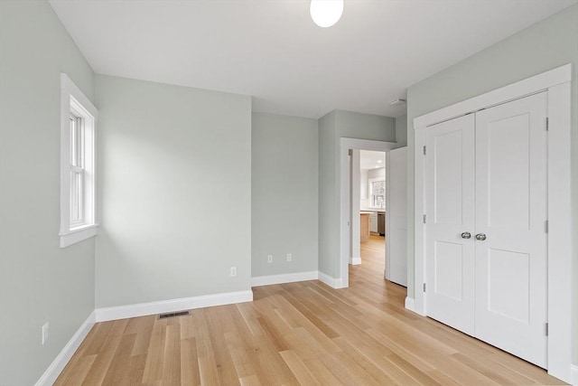 unfurnished bedroom featuring visible vents, baseboards, a closet, and light wood-style flooring