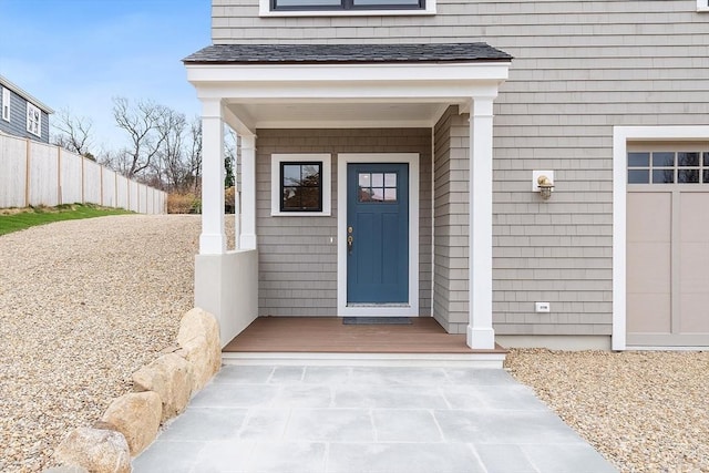 doorway to property featuring a porch, a shingled roof, and fence