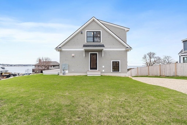 back of property featuring a lawn, entry steps, a water view, and fence