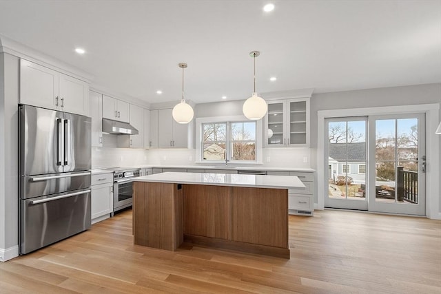 kitchen featuring light wood finished floors, a kitchen island, stainless steel appliances, light countertops, and under cabinet range hood