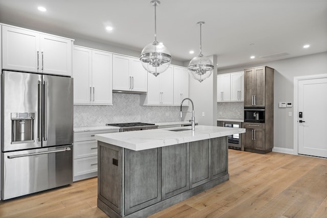 kitchen with high quality fridge, light hardwood / wood-style flooring, a center island with sink, and backsplash