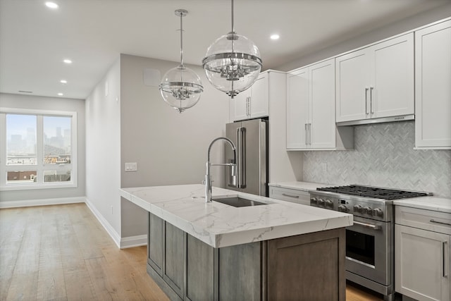 kitchen with decorative light fixtures, light hardwood / wood-style floors, a center island with sink, and premium appliances