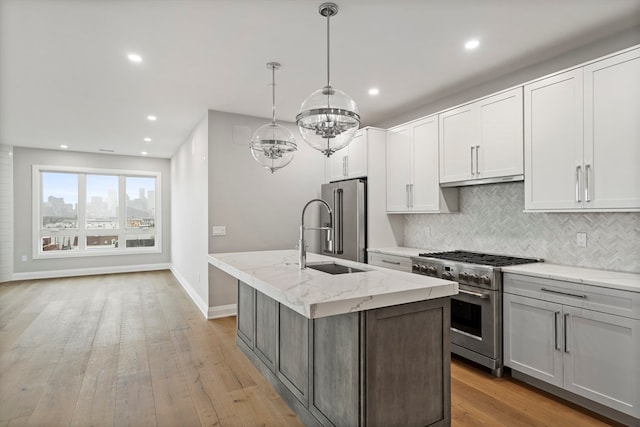 kitchen with light hardwood / wood-style flooring, a center island with sink, tasteful backsplash, premium appliances, and pendant lighting