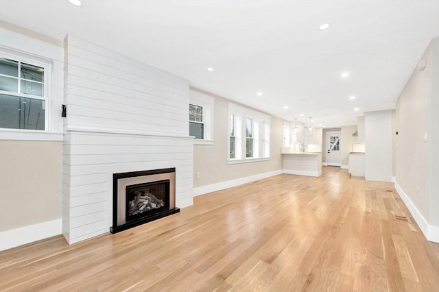 unfurnished living room with baseboards, light wood finished floors, a fireplace, and recessed lighting