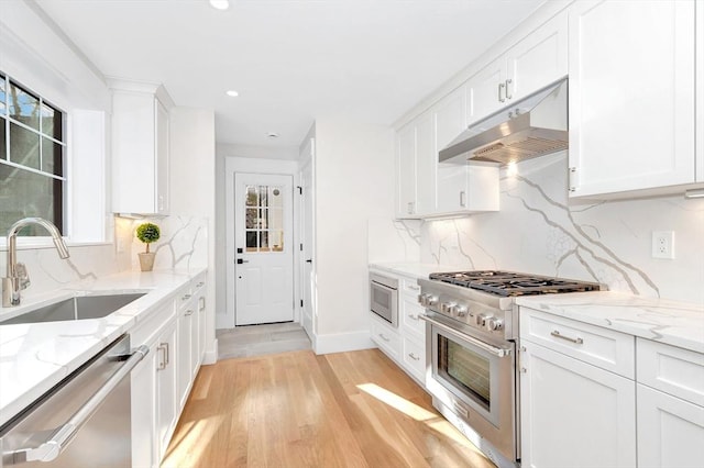 kitchen featuring appliances with stainless steel finishes, white cabinets, a sink, light stone countertops, and under cabinet range hood