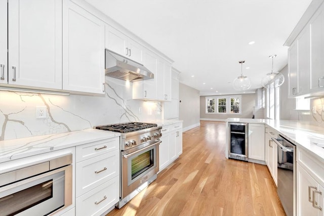 kitchen with white cabinets, wine cooler, appliances with stainless steel finishes, decorative light fixtures, and under cabinet range hood