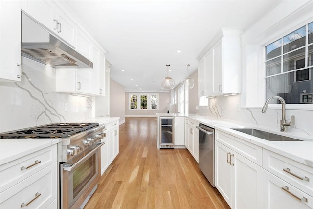 kitchen featuring stainless steel appliances, a sink, decorative light fixtures, and white cabinetry