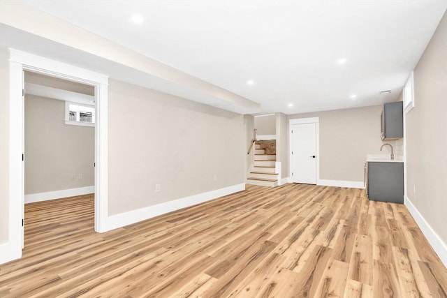 finished basement featuring light wood finished floors, stairway, a sink, and baseboards