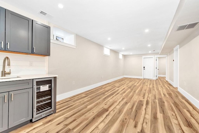 bar featuring beverage cooler, light wood-style flooring, a sink, and visible vents