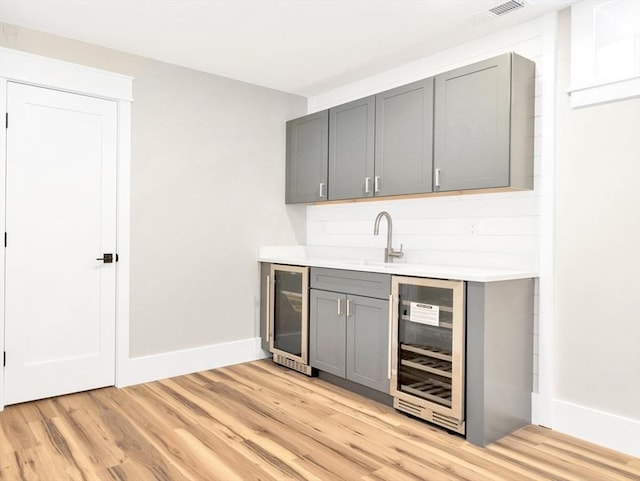 bar featuring beverage cooler, visible vents, a sink, and light wood-style flooring