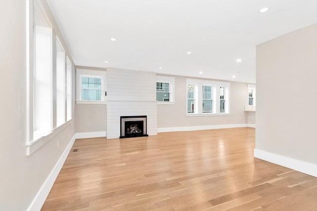 unfurnished living room featuring a large fireplace, recessed lighting, light wood-style flooring, and baseboards