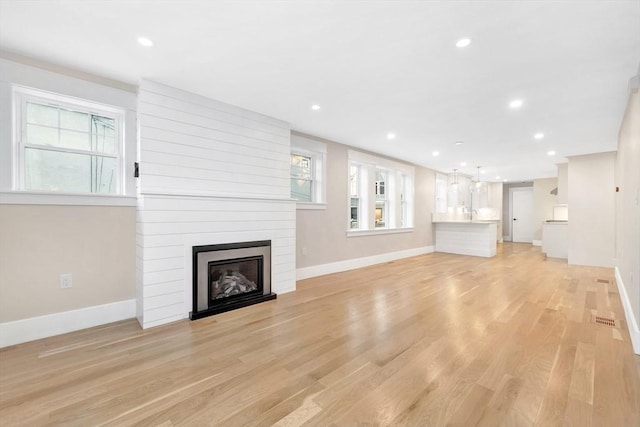 unfurnished living room featuring a healthy amount of sunlight, a fireplace, light wood-style flooring, and baseboards