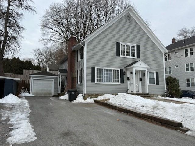 view of front of home featuring driveway, a detached garage, a chimney, and an outbuilding