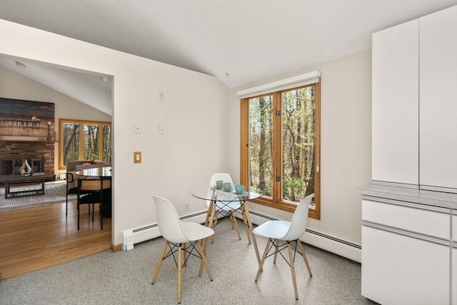 dining area with a healthy amount of sunlight, a baseboard radiator, a brick fireplace, and lofted ceiling