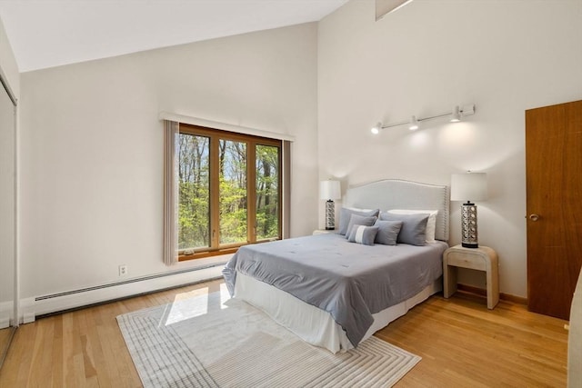 bedroom with high vaulted ceiling, baseboard heating, and light wood-type flooring