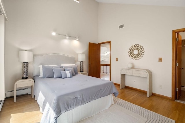 bedroom featuring visible vents, baseboards, light wood-style flooring, and a baseboard heating unit