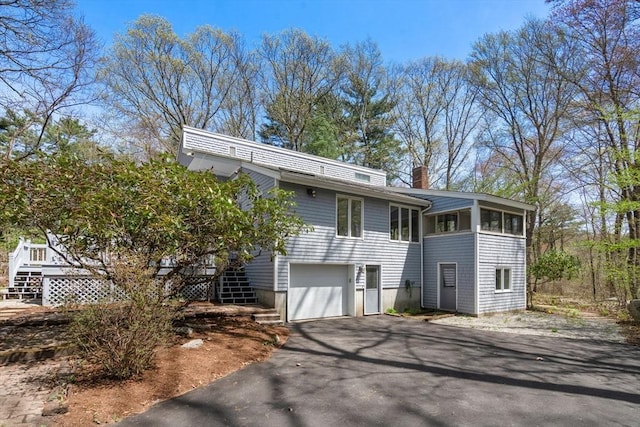 bi-level home with a chimney, stairs, a sunroom, an attached garage, and driveway