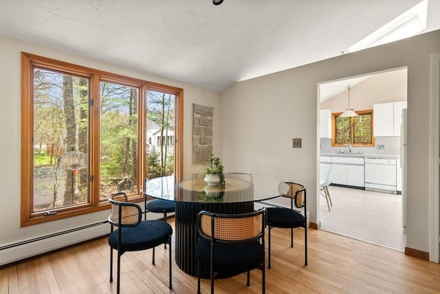 dining room featuring light wood-style floors, vaulted ceiling, and a baseboard heating unit