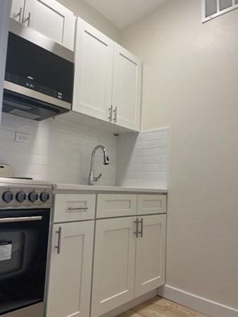 1258 Commonwealth Ave Unit 8, Boston, MA 02134 - kitchen featuring range with electric cooktop, stainless steel microwave, decorative backsplash, light wood-style floors, and baseboards