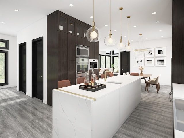 kitchen with light wood-type flooring, dark brown cabinets, a kitchen island, sink, and hanging light fixtures