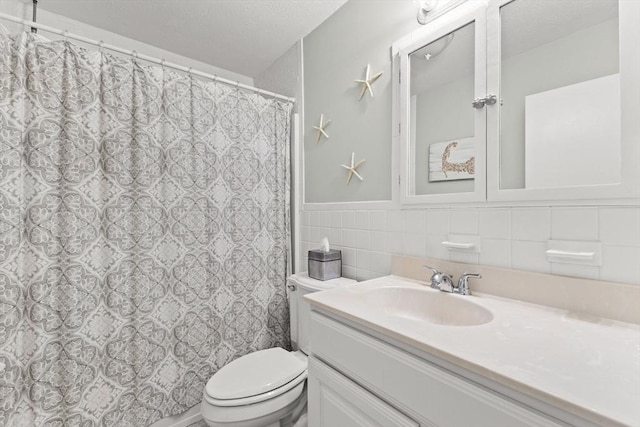 8 Stackpole Cir, Bourne, MA 02532 - bathroom with vanity, toilet, a textured ceiling, tile walls, and a wainscoted wall