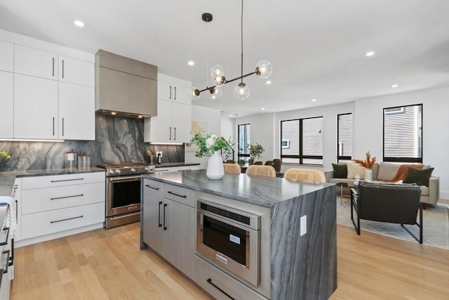 kitchen featuring pendant lighting, white cabinetry, high end stainless steel range oven, a center island, and wall chimney exhaust hood