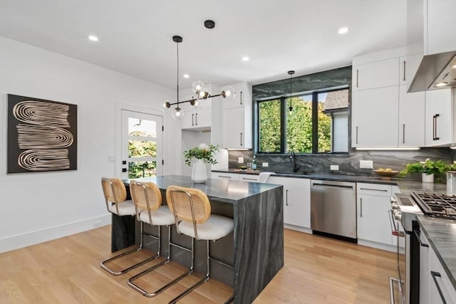 kitchen featuring appliances with stainless steel finishes, decorative light fixtures, white cabinets, a center island, and wall chimney range hood