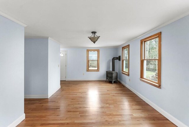 unfurnished room featuring baseboards, crown molding, light wood-style floors, and a wood stove