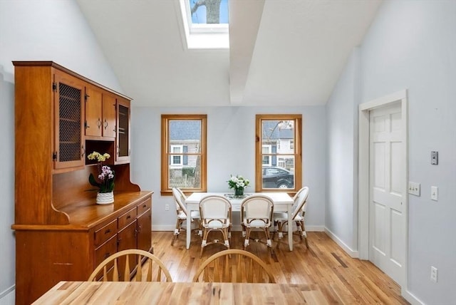 dining space with lofted ceiling with skylight, baseboards, and light wood-style flooring