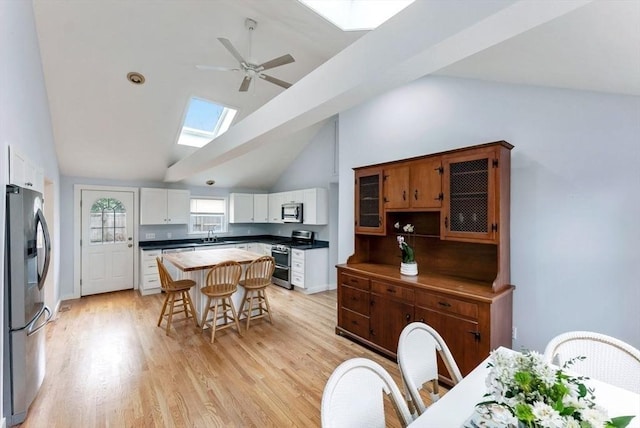 kitchen featuring stainless steel appliances, a kitchen island, a ceiling fan, light wood-type flooring, and a kitchen breakfast bar