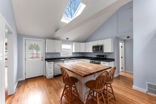 kitchen with a breakfast bar area, a sink, wood counters, visible vents, and appliances with stainless steel finishes