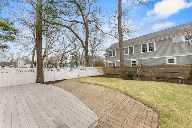 wooden deck featuring a fenced backyard, a lawn, a gate, and a patio area
