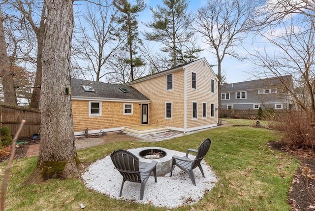 rear view of property with a fire pit, a lawn, and fence