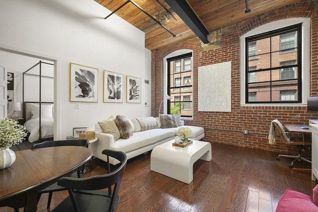 living room featuring dark wood-type flooring, beamed ceiling, brick wall, and wooden ceiling