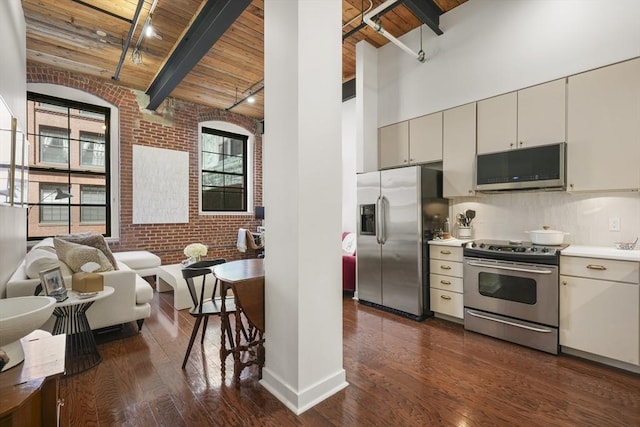 kitchen with brick wall, a towering ceiling, dark hardwood / wood-style floors, stainless steel appliances, and wooden ceiling