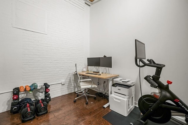 home office with brick wall and dark hardwood / wood-style floors