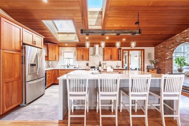 kitchen featuring light countertops, decorative backsplash, wood ceiling, wall chimney range hood, and stainless steel fridge