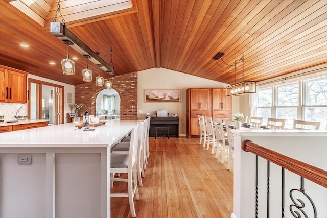 kitchen with tasteful backsplash, a spacious island, vaulted ceiling, light countertops, and light wood-type flooring