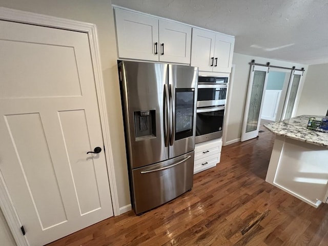 kitchen featuring appliances with stainless steel finishes, white cabinetry, dark hardwood / wood-style flooring, light stone counters, and a barn door