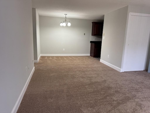 carpeted empty room featuring a textured ceiling, baseboards, and a chandelier