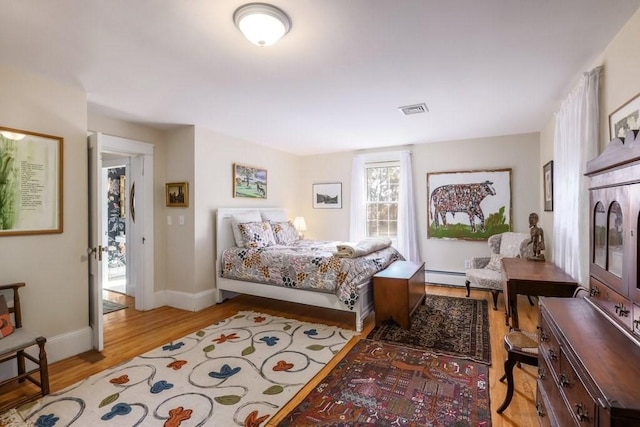 bedroom with light hardwood / wood-style floors and a baseboard heating unit