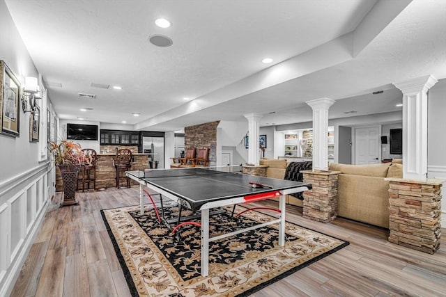 14 Glen Rd, Hopkinton, MA 01748 - playroom featuring ornate columns, light wood finished floors, a wainscoted wall, a bar, and a decorative wall