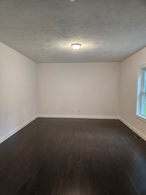 unfurnished room with a textured ceiling and dark wood-type flooring