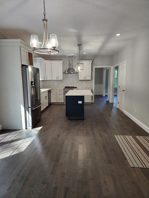 kitchen with pendant lighting, high end appliances, a kitchen island, wall chimney range hood, and white cabinetry