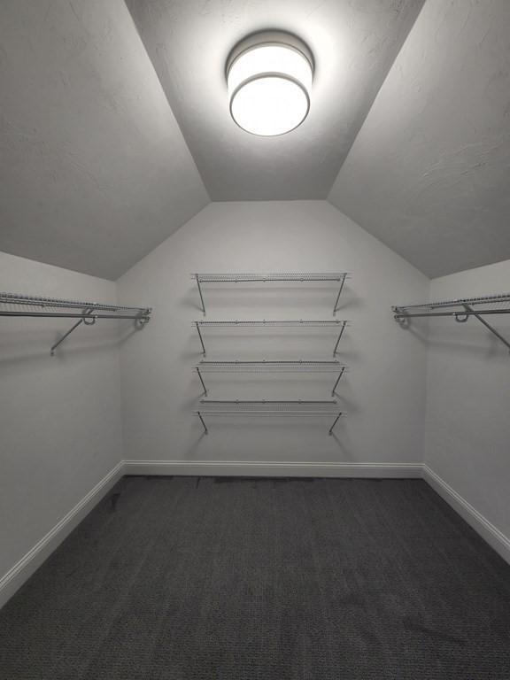 walk in closet with dark colored carpet and vaulted ceiling