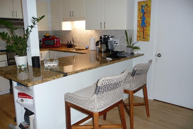 kitchen with sink, decorative backsplash, dark stone countertops, kitchen peninsula, and a breakfast bar area