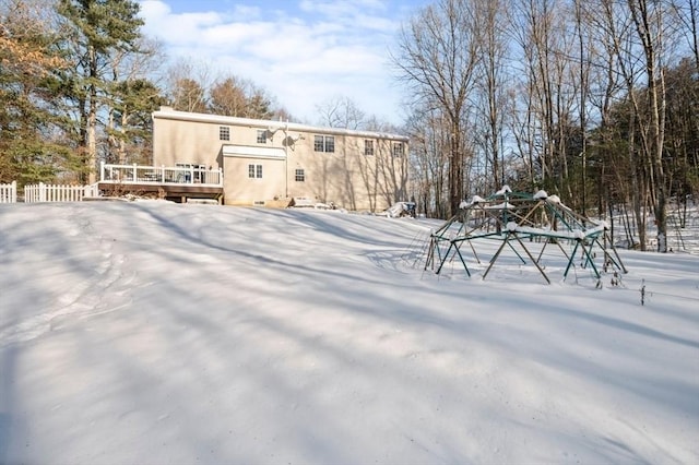 snow covered back of property featuring stucco siding, fence, and a deck