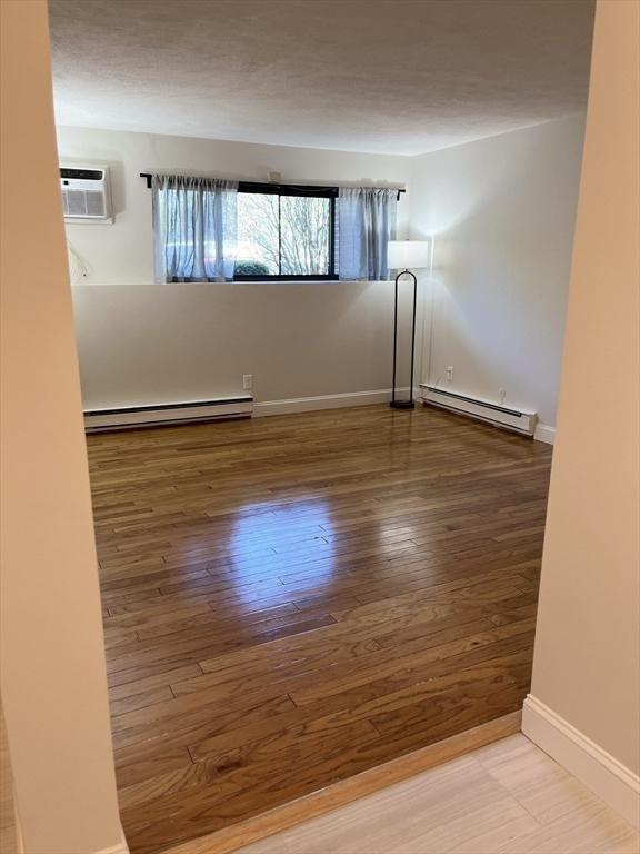 spare room with baseboards, a baseboard radiator, a wall unit AC, and wood finished floors